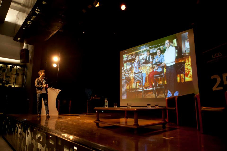 Francisco Sáez en escena durante De Cero a CEO en la Universidad del Desarrollo, con living de escenario y pantalla al fondo.